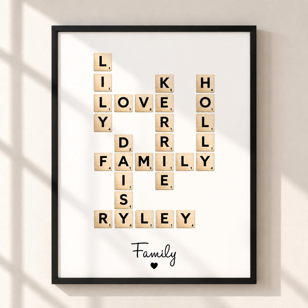 A framed personalized Scrabble-style wall art print hangs on a light beige wall. The black frame contains a white background with wooden letter tiles arranged to spell out family words, and the word 'Family' appears at the bottom with a small heart.