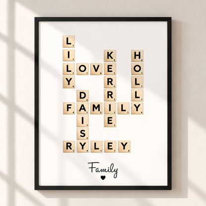 A framed personalized Scrabble-style wall art print hangs on a light beige wall. The black frame contains a white background with wooden letter tiles arranged to spell out family words, and the word 'Family' appears at the bottom with a small heart.