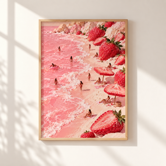 A framed art print depicting a whimsical pink beach scene with strawberries, beach umbrellas, and tiny people in the water, hung on a light beige wall with soft window shadows.