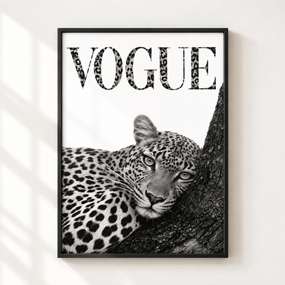 A framed black and white art print featuring a leopard resting on a tree trunk with the word 'VOGUE' in leopard-print lettering, displayed on a light wall with soft window shadow patterns.