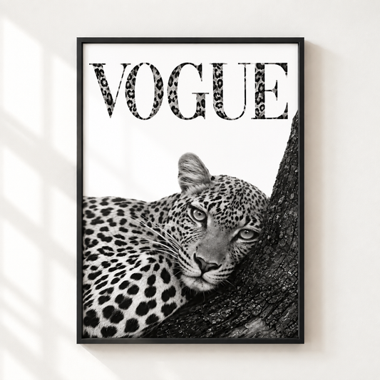 A framed black and white art print featuring a leopard resting on a tree trunk with the word 'VOGUE' in leopard-print lettering, displayed on a light wall with soft window shadow patterns.