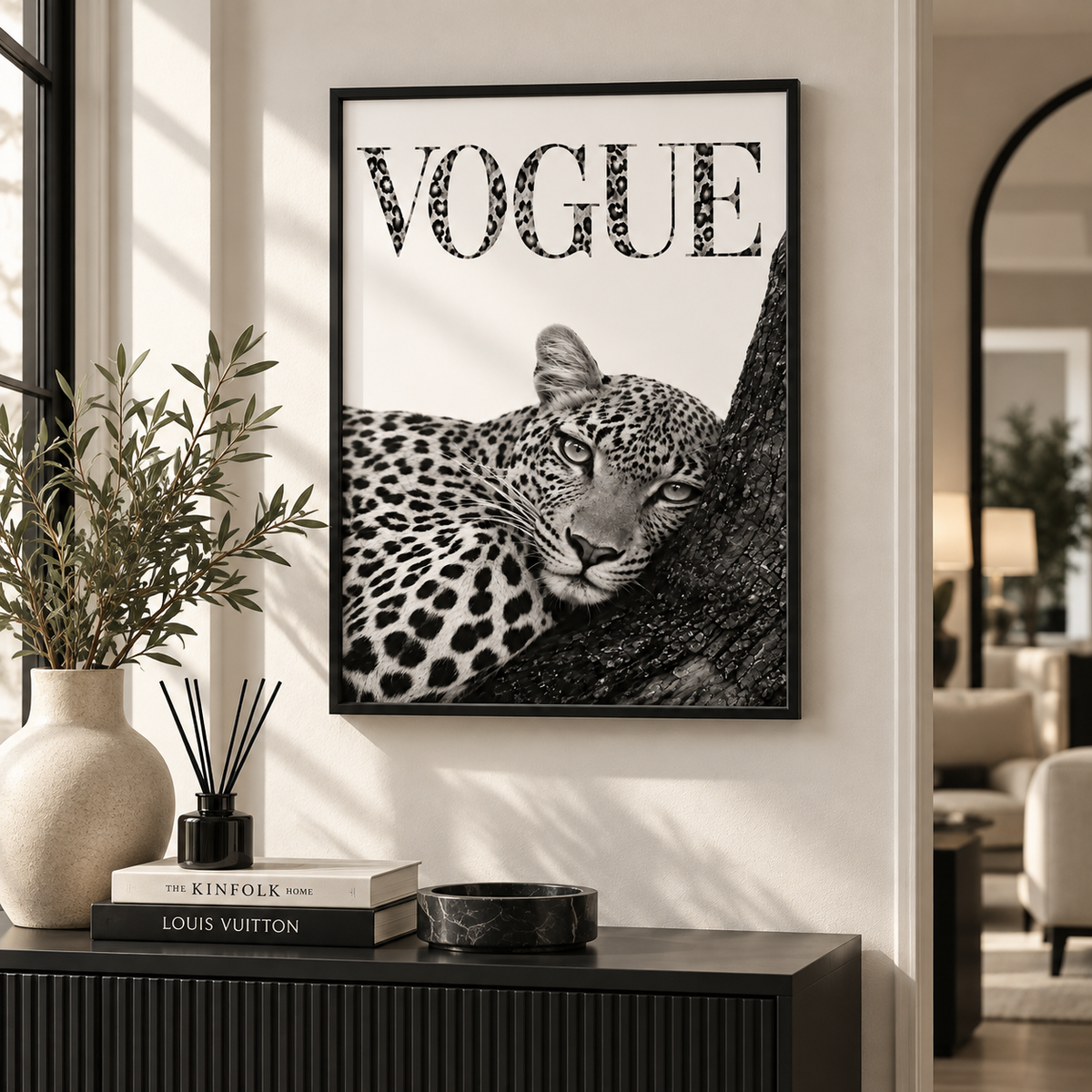 A framed black and white art print featuring a leopard and the word 'VOGUE' in leopard-print lettering, displayed on a wall above a console table in a modern interior setting.