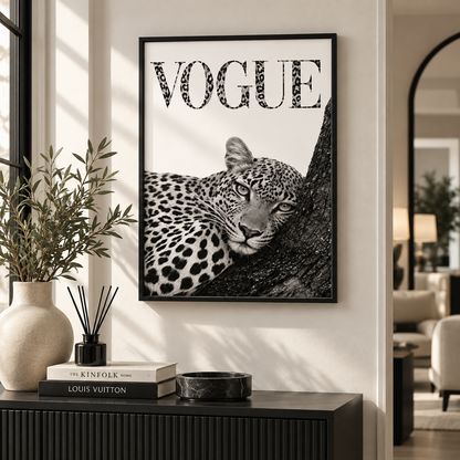 A framed black and white art print featuring a leopard and the word 'VOGUE' in leopard-print lettering, displayed on a wall above a console table in a modern interior setting.