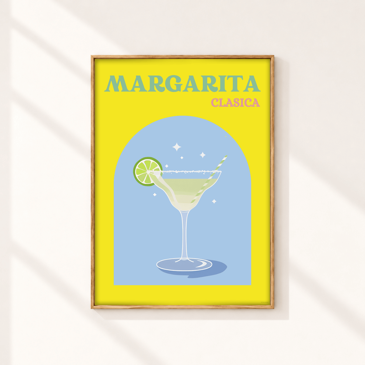 A framed art print featuring a retro-style illustration of a margarita cocktail with the text 'MARGARITA CLASICA' on a bright yellow background, hanging on a light wall with soft diagonal shadows.