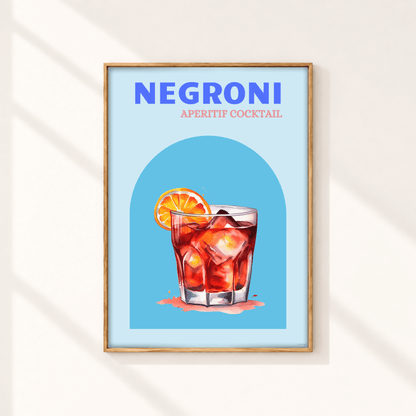 A framed art print featuring a stylized illustration of a Negroni aperitif cocktail with a blue background and a light wood frame, displayed on a warm off-white wall with soft diagonal shadows.