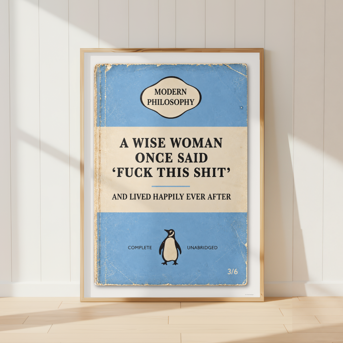 A framed book-cover-style poster leaning against a white paneled wall on a light wood floor. The artwork mimics a vintage Penguin Classics cover with a blue background, cream title band, black text, and a small penguin illustration.