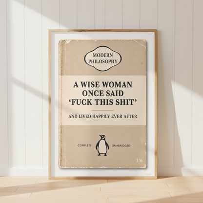 A framed book-style poster leaning against a white paneled wall on a light wood floor. The poster has a vintage beige cover design with the text 'A WISE WOMAN ONCE SAID 'FUCK THIS SHIT' AND LIVED HAPPILY EVER AFTER' and a small Penguin logo near the bottom.