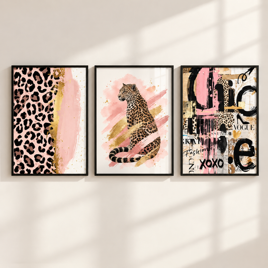 Three framed wall art prints hang side by side on a light beige wall with soft window-shadow lighting. The left print shows a leopard print and pink brushstroke design, the center print shows a seated leopard on pink and gold abstract strokes, and the right print is a collage with leopard elements, black typography, and pink accents.