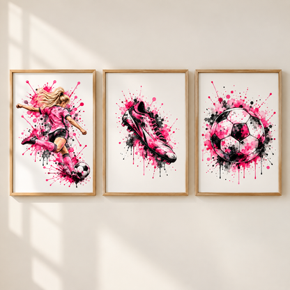 Three framed wall art prints with pink, black, and white soccer-themed watercolor designs hang on a light beige wall. The left print shows a soccer player kicking a ball, the center shows a soccer cleat, and the right shows a soccer ball.