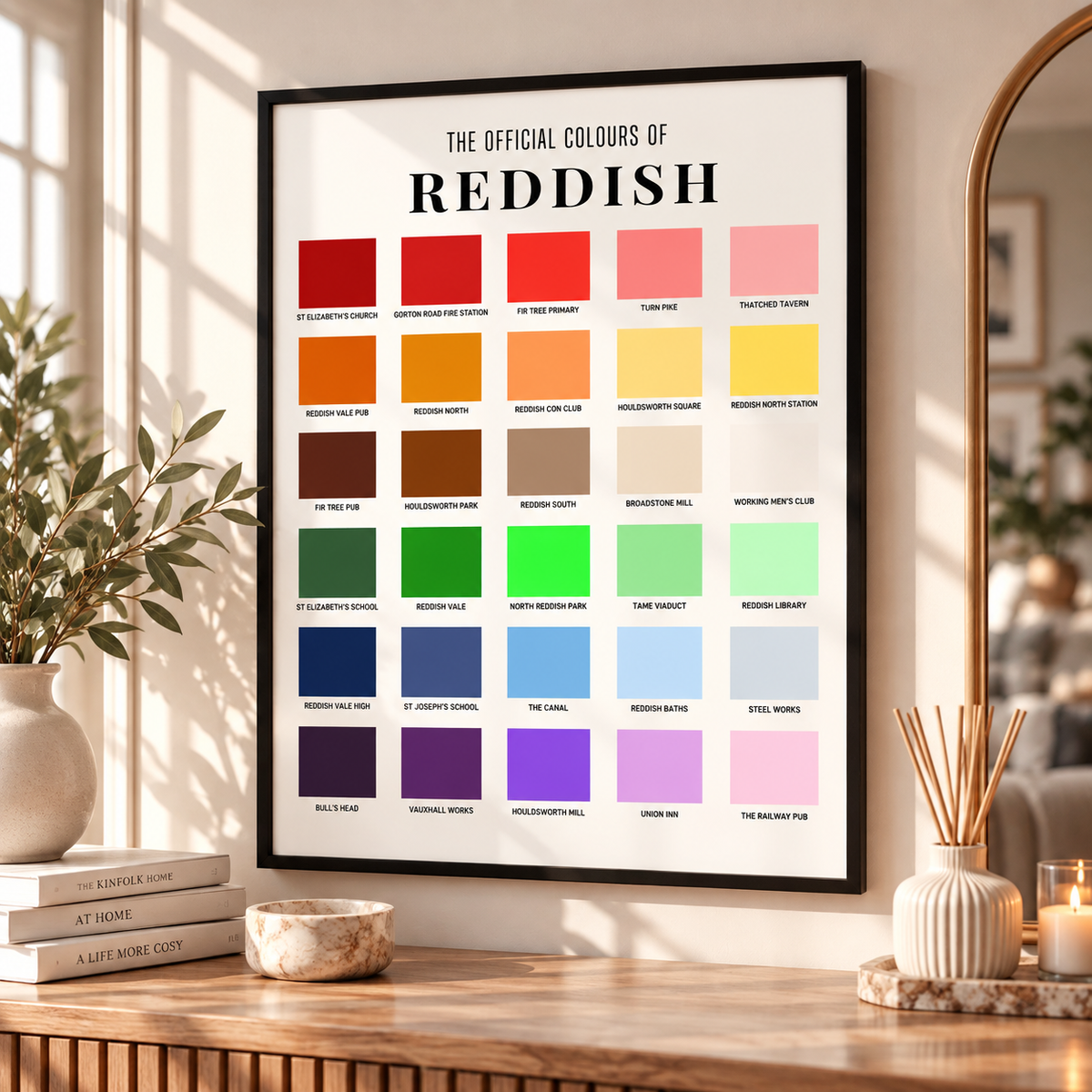 A framed poster titled 'THE OFFICIAL COLOURS OF REDDISH' hangs on a wall in a styled interior. The print shows many color blocks labeled with different shades of reddish tones, ranging from red and orange to green, blue, purple, and pink.