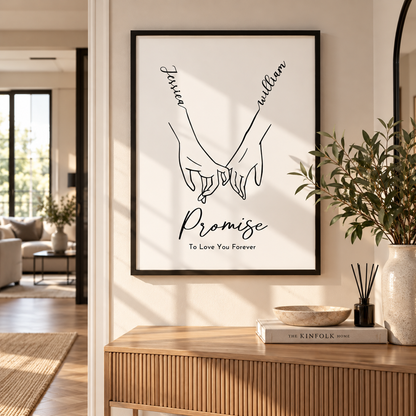 A framed black-and-white art print hanging on a beige wall in a modern living space. The print features two hands holding, with the words 'faith' and 'william' above and 'Promise To Love You Forever' below in elegant script.