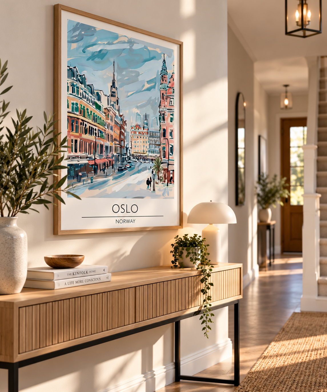A framed art print of Oslo, Norway, featuring a colorful impressionistic cityscape, displayed on a light wood console table in a beautifully styled modern hallway.