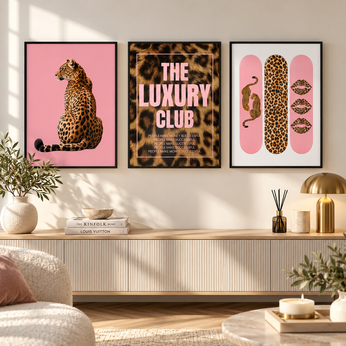 Three framed wall art prints with a cohesive pink and leopard-print theme hang above a console table in a styled living room. The left print shows a seated leopard on pink, the center reads 'THE LUXURY CLUB' with a leopard pattern background, and the right print features pink panels with a leopard motif and lipstick kiss marks.