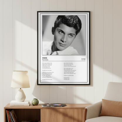 A framed black-and-white poster of Paul Anka's song 'Diana' leaning against a white paneled wall on a light wood floor, with soft window shadows cast across the scene.