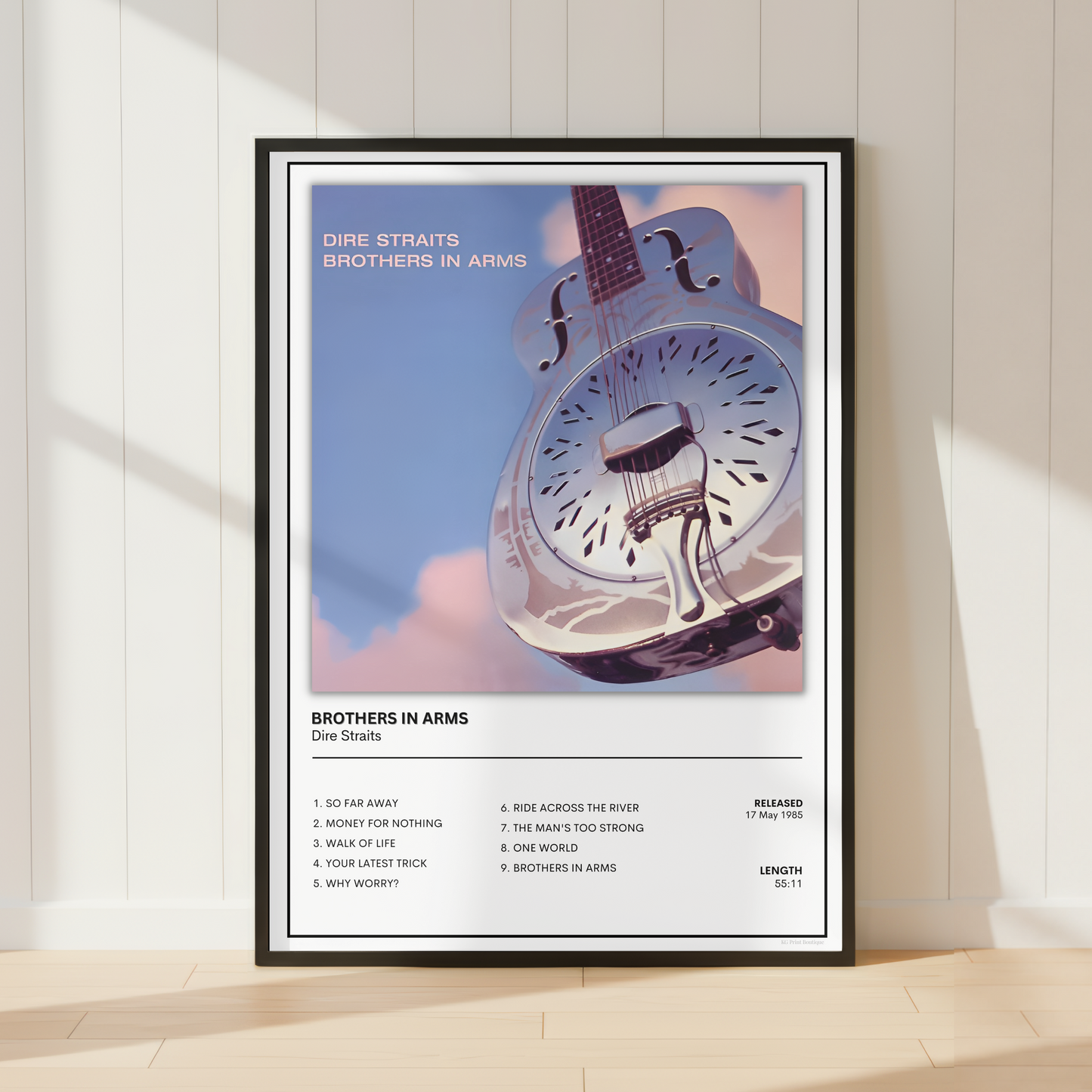 A framed music poster of Dire Straits' 'Brothers in Arms' leaning against a white paneled wall on a light wood floor, with soft window shadows cast across the scene.