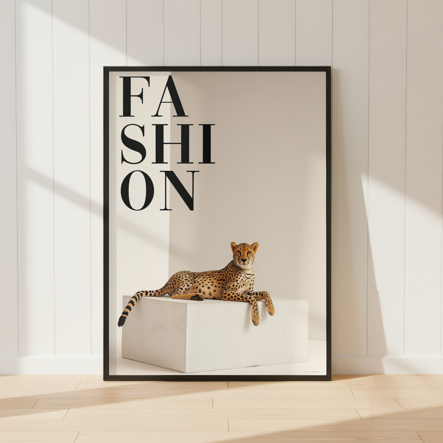 A framed fashion poster leaning against a white paneled wall on a light wood floor. The poster features the word 'FASHION' in large black letters above a spotted leopard lying on a white block.