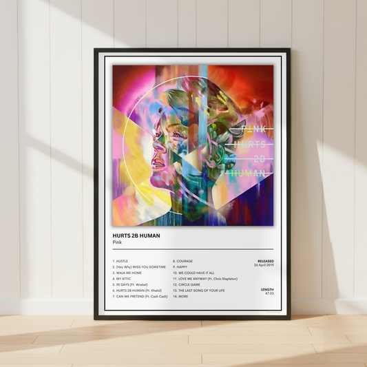 A framed music poster for Pink's album 'HURTS 28 HUMAN' leaning against a white paneled wall on a light wood floor, with colorful abstract artwork and tracklist details.