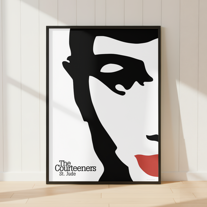 A framed art print of The Courteeners St. Jude, featuring a bold black and white graphic portrait with a red accent, leaning against a white paneled wall on a light wood floor.