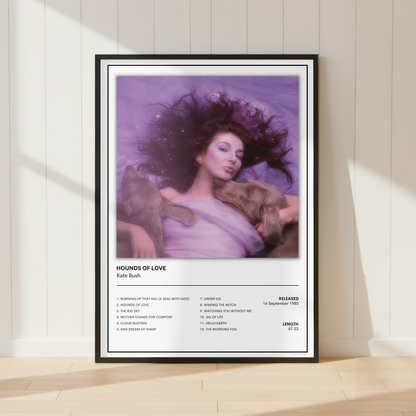 A framed music poster of Kate Bush's 'Hounds of Love' leaning against a white paneled wall on a light wood floor, styled with soft window shadows.
