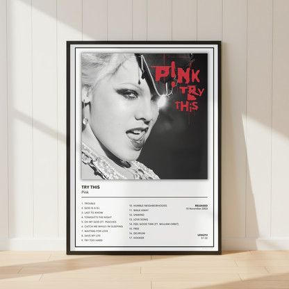A framed music poster of Pink's album 'Try This' leaning against a white paneled wall on a light wood floor, with soft window shadows cast across the scene.