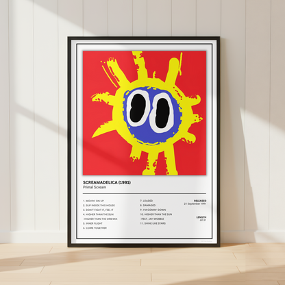 A framed art print of Primal Scream Screamadelica' poster, featuring a bold yellow sun with a blue face on a red background, displayed in a black frame against a white paneled wall on a light wood floor.