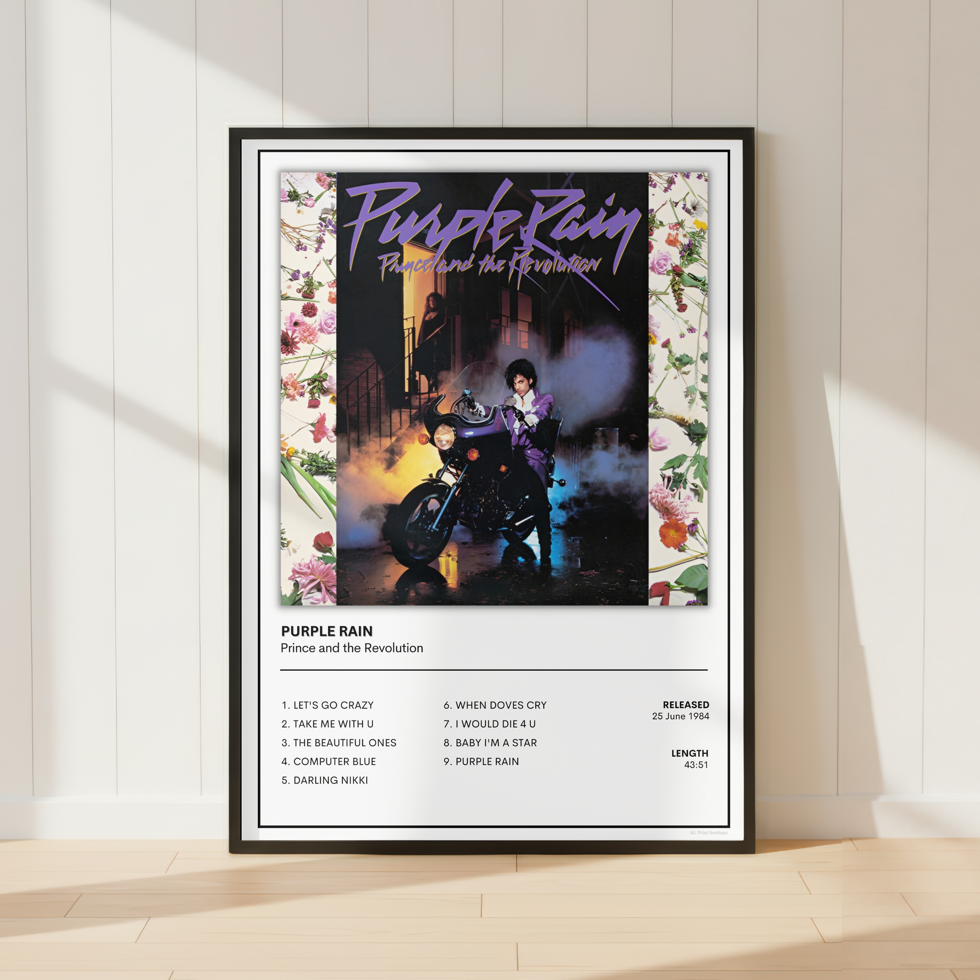 A framed music poster of Prince, Purple Rain leaning against a white paneled wall on a light wood floor, with soft sunlight casting shadows across the scene.