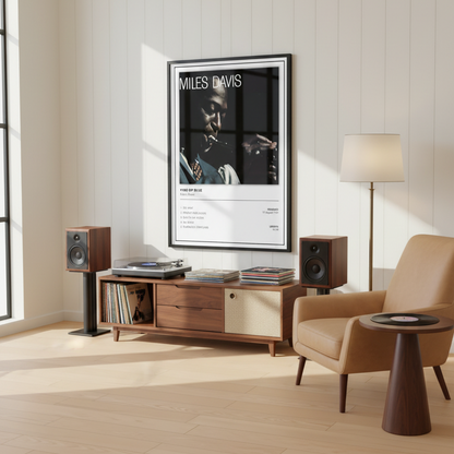 A framed Miles Davis 'Kind of Blue' music poster leaning against a white paneled wall on a light wood floor, with soft sunlight casting shadows across the scene.