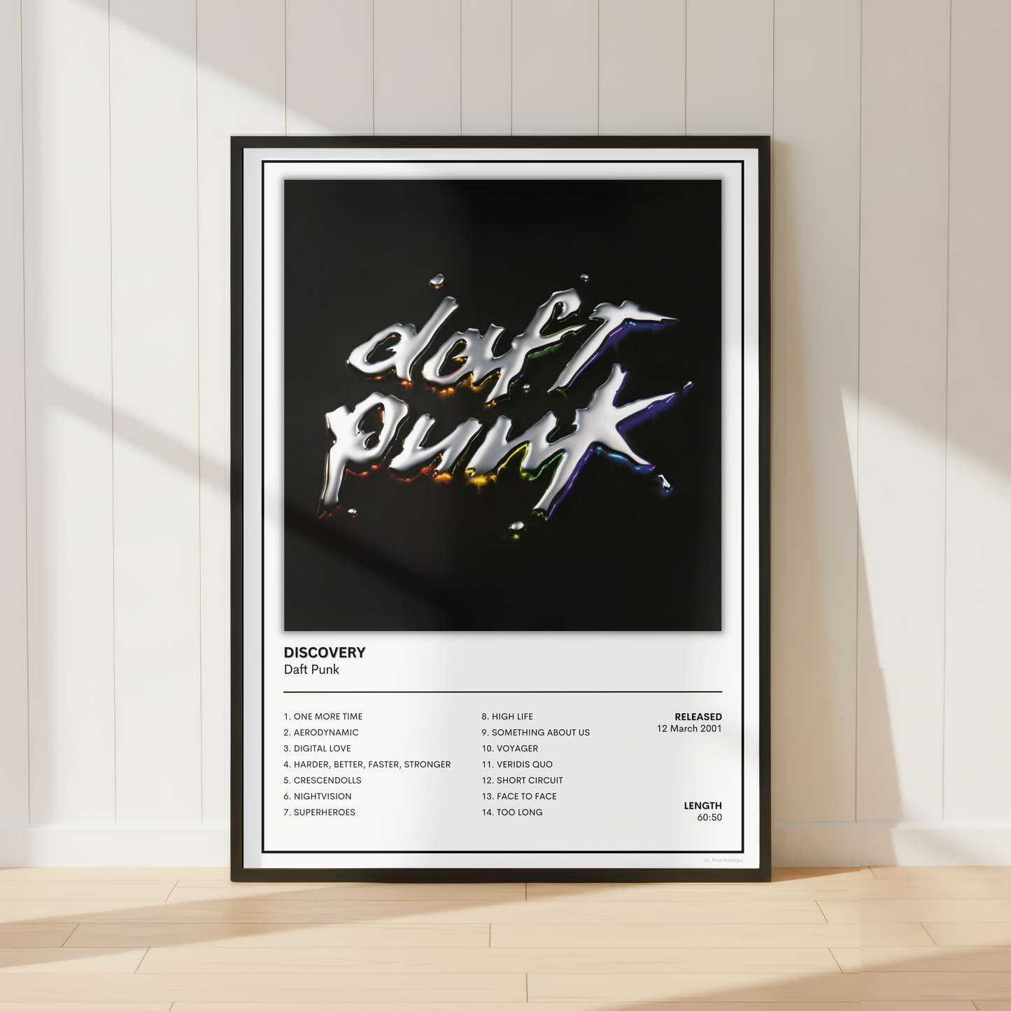 A framed music poster for Daft Punk's album 'Discovery' leaning against a white paneled wall on a light wood floor, with soft window shadows cast across the scene.
