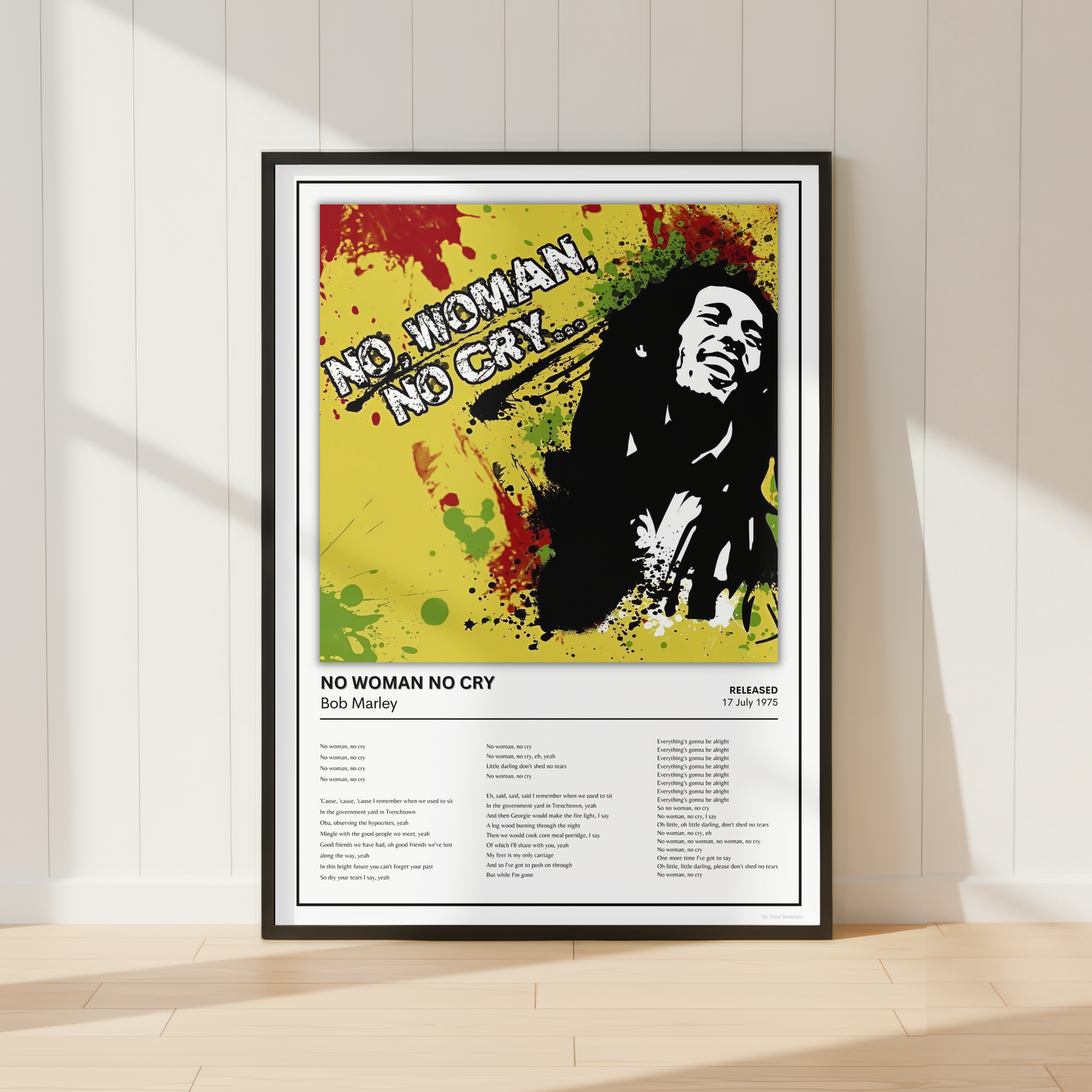 A framed Bob Marley 'No Woman No Cry' poster leaning against a white paneled wall on a light wood floor, with soft window shadows cast across the scene.