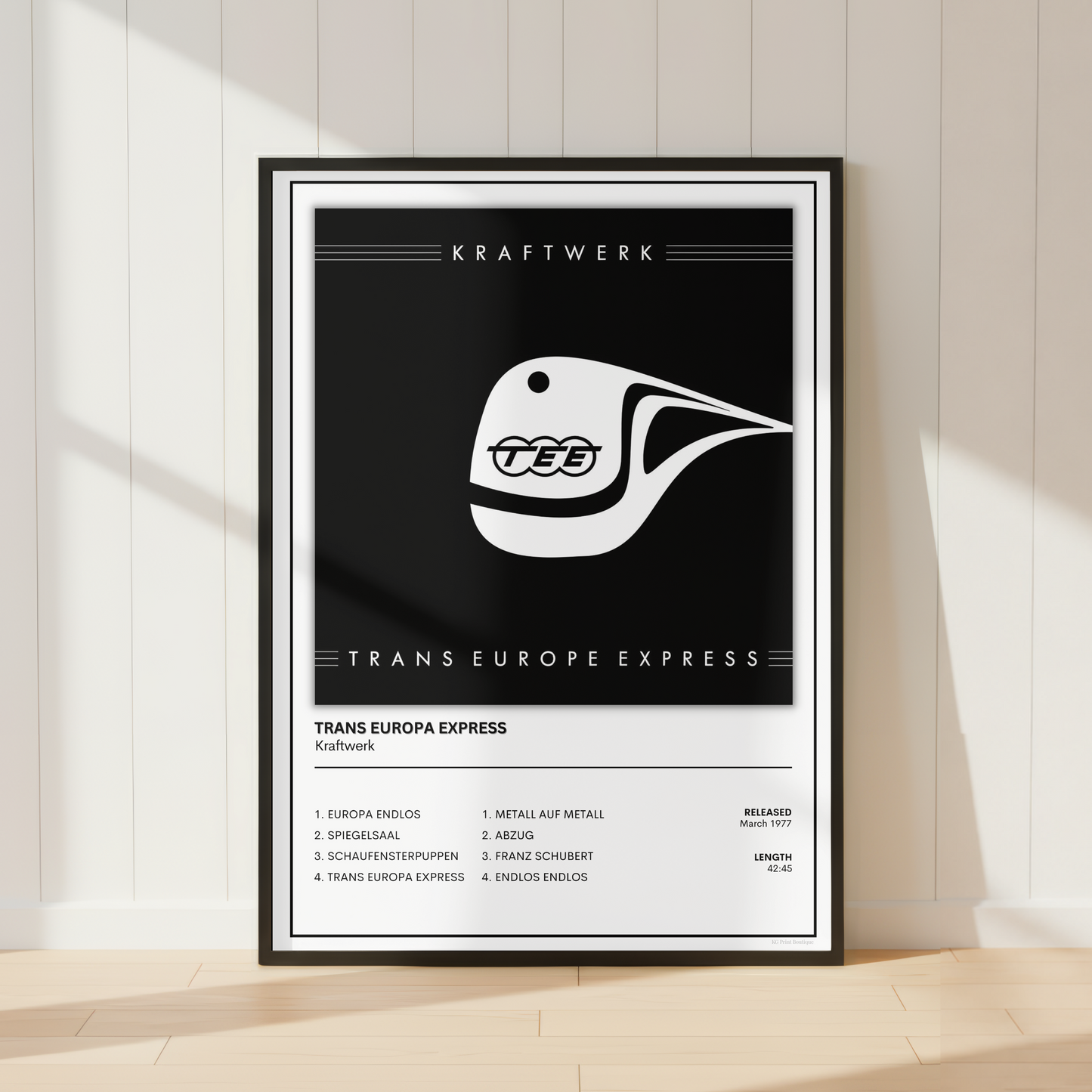 A framed black and white poster featuring the Trans Europe Express train logo and route text, leaning against a white paneled wall on a light wood floor.