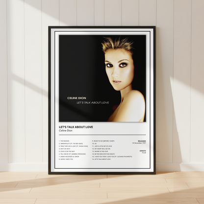 A framed music poster of Celine Dion's 'Let's Talk About Love' leaning against a white paneled wall on a light wood floor.