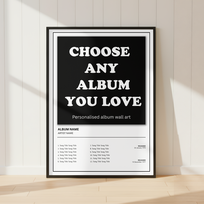 A framed personalized album wall art print leaning against a white paneled wall on a light wood floor. The poster has a black background with large white text reading 'CHOOSE ANY ALBUM YOU LOVE' and a track list section below.