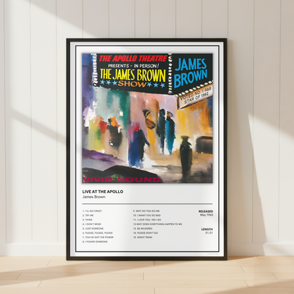 A framed concert poster for James Brown's 'Live at the Apollo' is displayed leaning against a white paneled wall on a light wood floor. The poster features a colorful painted performance scene with audience members and a black-framed tracklist section below.