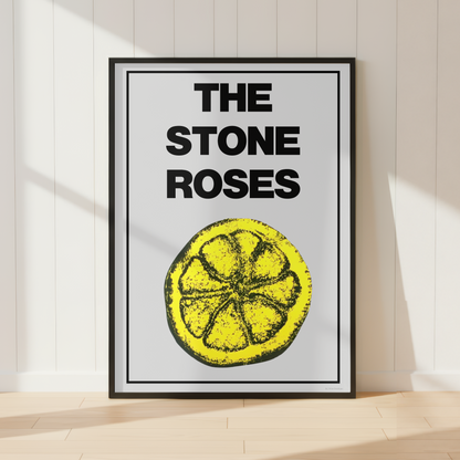 A framed art print featuring the text 'THE STONE ROSES' above a yellow lemon slice illustration, leaning against a white paneled wall on a light wood floor.