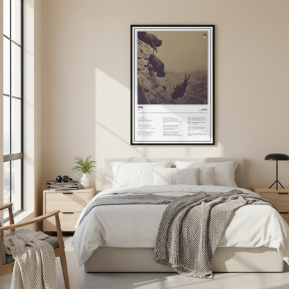 A framed art print featuring a sepia-toned photograph of three sheep on a rocky cliffside with printed text below, leaning against a white paneled wall on a light wood floor.