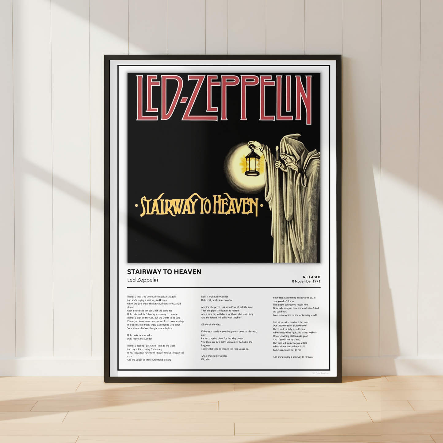 A framed Led Zeppelin 'Stairway to Heaven' poster leaning against a white paneled wall on a light wood floor, with soft window shadows cast across the scene.