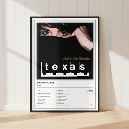 A framed music poster for 'White On Blonde' by Texas stands against a white paneled wall on a light wood floor, with soft sunlight casting shadows.