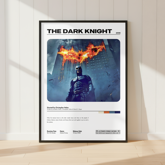 A framed 'The Dark Knight' movie poster leaning against a white paneled wall on a light wood floor, with warm sunlight casting shadows across the scene.