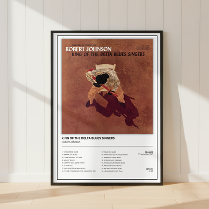 A framed Robert Johnson 'King of the Delta Blues Singers' poster leaning against a white paneled wall on a light wood floor, with soft sunlight casting shadows.