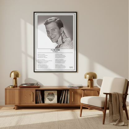 A framed black-and-white Pat Boone 'I'll Be Home' music poster is displayed leaning against a white paneled wall on a light wood floor, with soft window shadows cast across the scene.