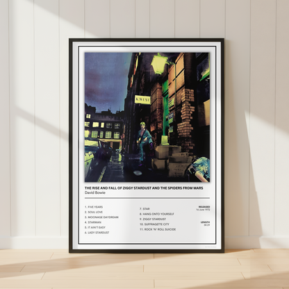 A framed music poster of David Bowie's 'The Rise and Fall of London Standout' leaning against a white paneled wall on a light wood floor.