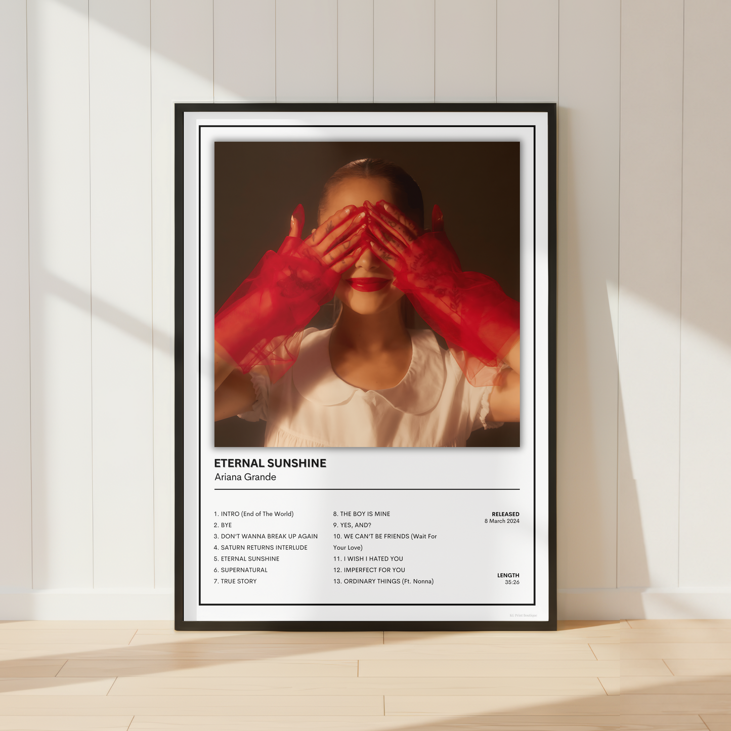 A framed music poster for Arijit Singh's song 'Eternal Sunshine' leaning against a white paneled wall on a light wood floor, with warm sunlight casting shadows.