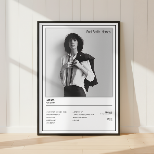 A framed black and white music poster of Patti Smith's album 'Horses' leaning against a cream-colored paneled wall on a light wood floor.