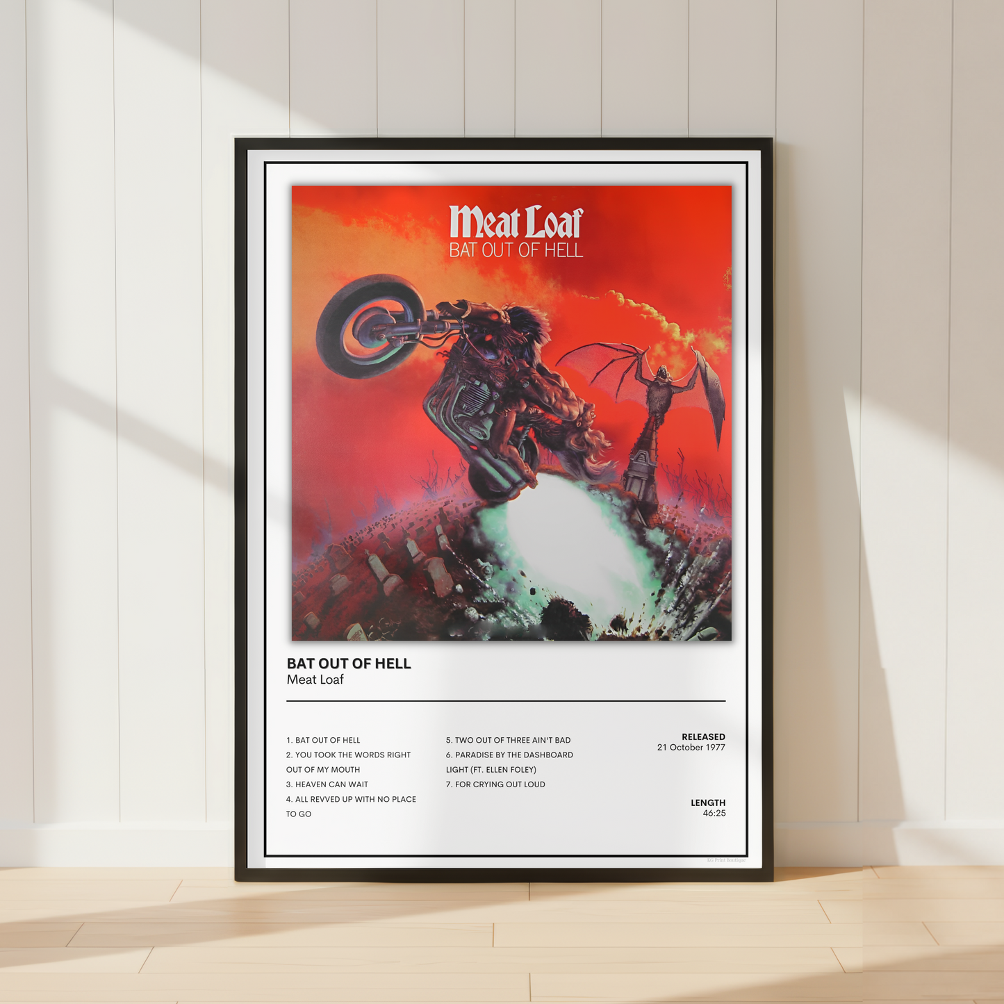 A framed poster of the Meat Loaf's album 'Bat Out of Hell' leaning against a white paneled wall on a light wood floor, with soft window shadows cast across the scene.