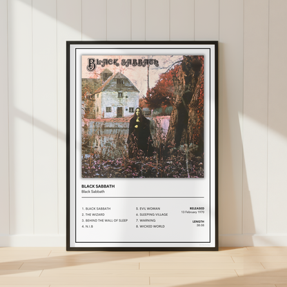 A framed Black Sabbath music poster leaning against a white paneled wall on a light wood floor, with soft sunlight casting shadows across the scene.