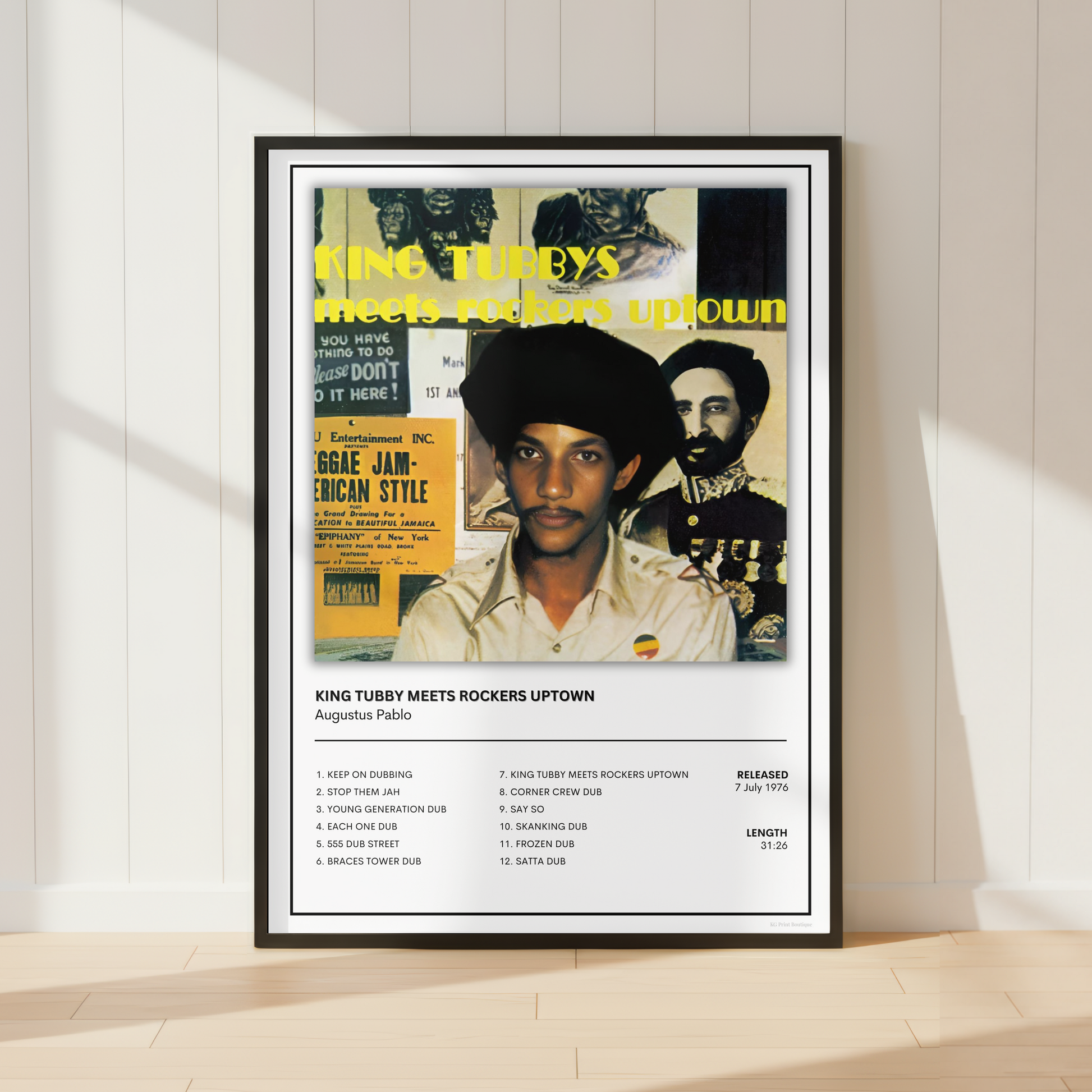 A framed music poster of King Tubby featuring a collage-style portrait and tracklist, leaning against a white paneled wall on a light wood floor.