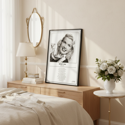 A framed black-and-white music poster of Doris Day's song 'Secret Love' leaning against a white paneled wall on a light wood floor.
