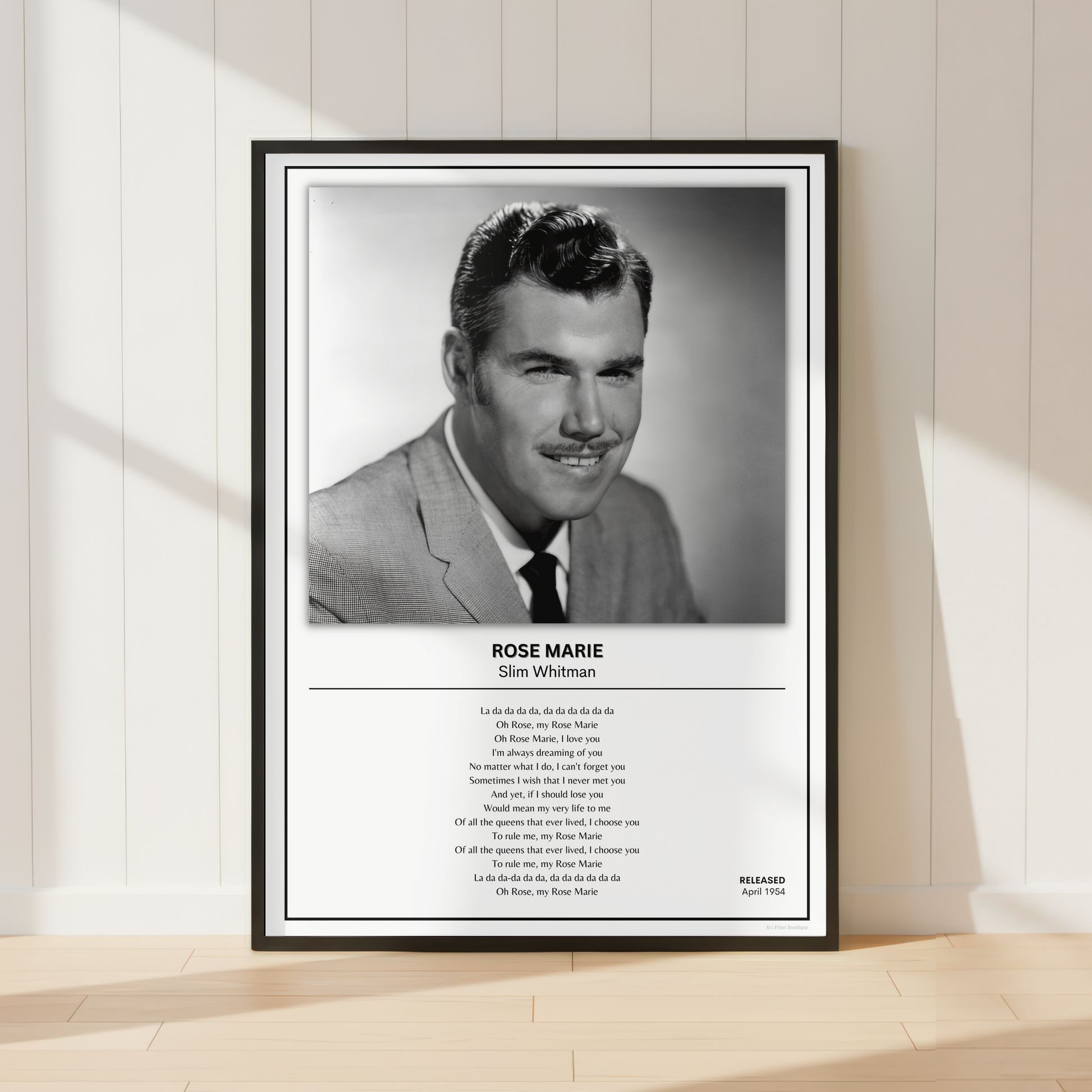 A framed black-and-white portrait print of Rose Marie as Slim Whitman leaning against a white paneled wall on a light wood floor. The print includes a black frame, a black-and-white photo, the name and role, and a block of small text below.