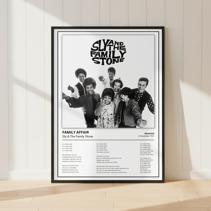 A framed black-and-white music poster for Sly and the Family Stone's 'Family Affair' leaning against a white paneled wall on a light wood floor, with soft window shadows cast across the scene.