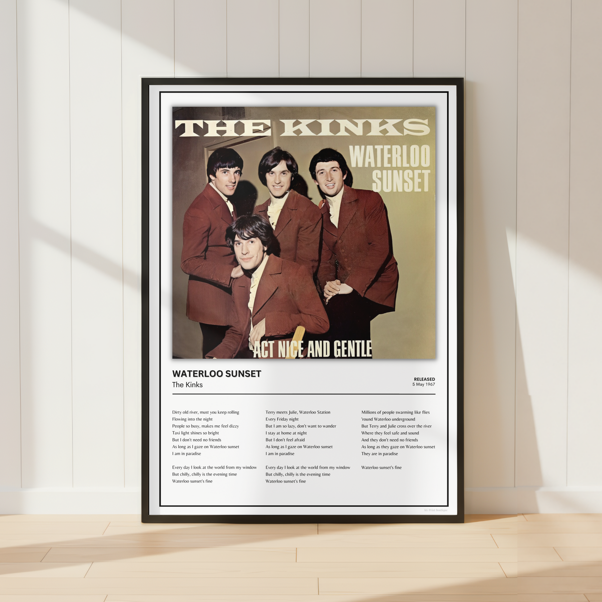 A framed music poster of The Kinks' 'Waterloo Sunset' leaning against a white paneled wall on a light wood floor, with soft window shadows cast across the scene.